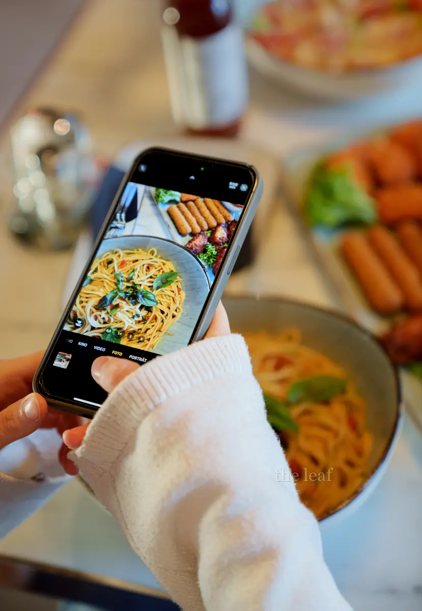 Eine Person fotografiert Pasta und Fingerfood am Tisch im The Leaf